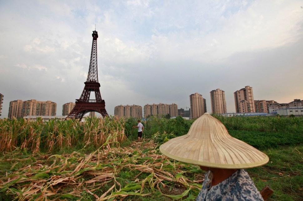 A farmer walks through a field near a replica of the Eiffel Tower at the Tianducheng development August 1, 2013. (REUTERS/Aly Song)
